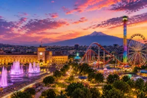 Evening view of Yerevan with Republic Square fountains, amusement park attractions, and Mount Ararat at sunset