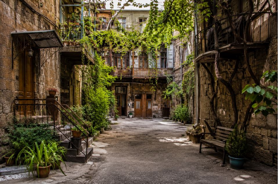 Historic hidden courtyard in Yerevan with stone buildings, wooden balconies and grapevines