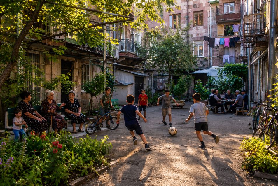 Children playing football in a traditional Yerevan courtyard surrounded by neighbors and historic apartment buildings